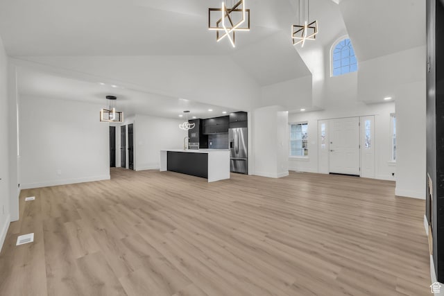 unfurnished living room featuring baseboards, a chandelier, light wood-style floors, visible vents, and high vaulted ceiling