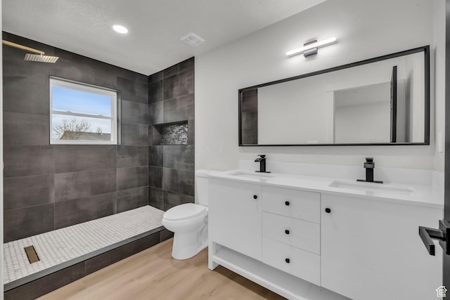 bathroom with tiled shower, a sink, toilet, and wood finished floors