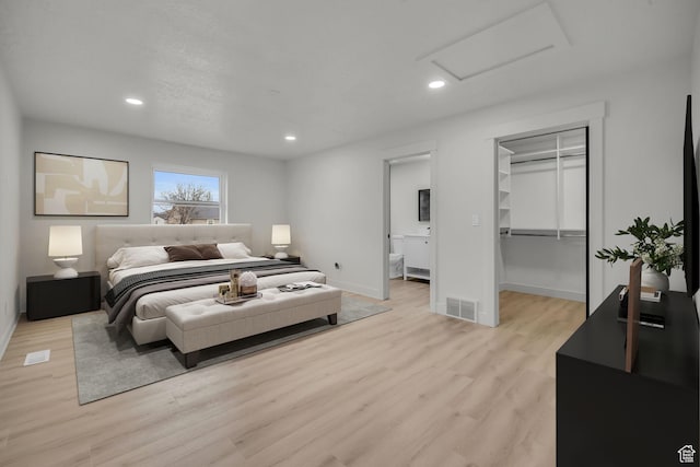 bedroom with light wood-style flooring, visible vents, recessed lighting, attic access, and a walk in closet
