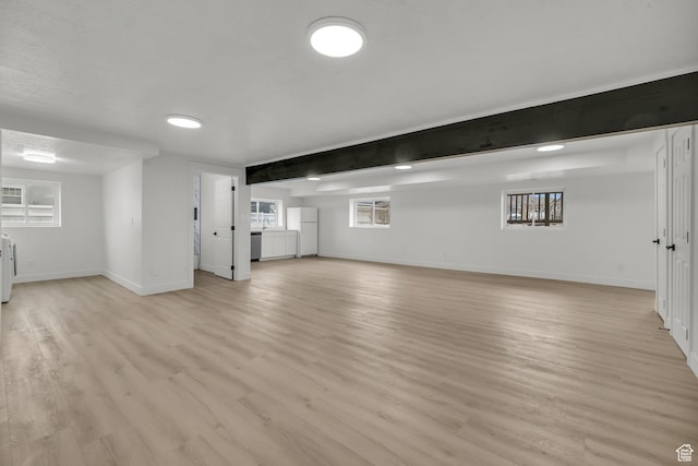 basement featuring light wood-type flooring, baseboards, and freestanding refrigerator