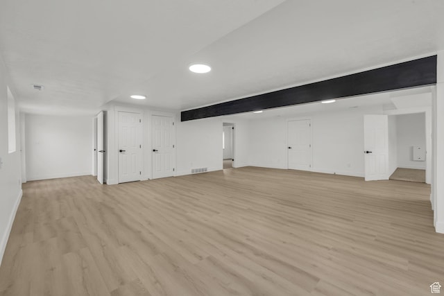 finished below grade area with light wood finished floors, visible vents, and baseboards