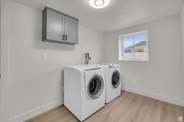 clothes washing area featuring light wood-style floors, a textured ceiling, washer and dryer, baseboards, and cabinet space