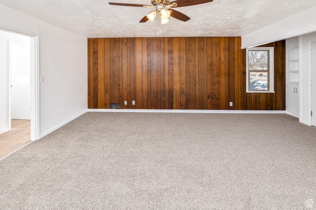 carpeted empty room featuring wooden walls and a textured ceiling