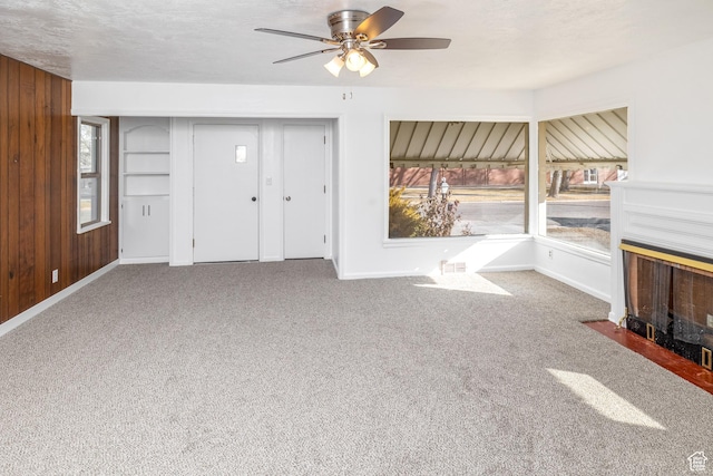 unfurnished living room featuring ceiling fan, wooden walls, carpet, and a textured ceiling