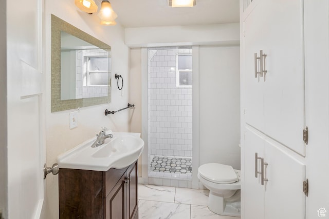 bathroom with a tile shower, vanity, and toilet