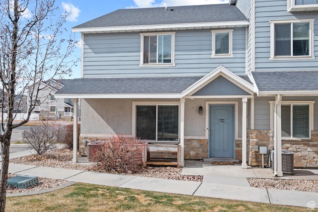 view of front facade featuring stone siding, stucco siding, central air condition unit, and roof with shingles
