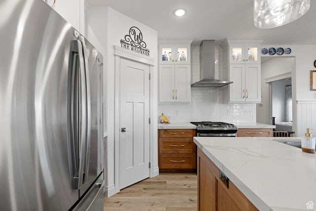 2418 W 4975 N, Cedar City, UT 84721 - kitchen with wall chimney range hood, backsplash, stainless steel appliances, white cabinets, and light wood-type flooring