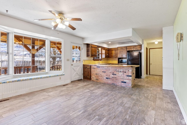 kitchen featuring sink, kitchen peninsula, black fridge, a textured ceiling, and light hardwood / wood-style flooring