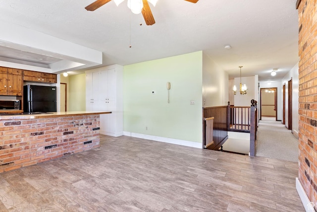 living room with a tray ceiling, ceiling fan with notable chandelier, light hardwood / wood-style floors, and a textured ceiling