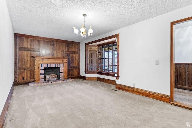 unfurnished living room with wooden walls, a notable chandelier, a fireplace, a textured ceiling, and light carpet