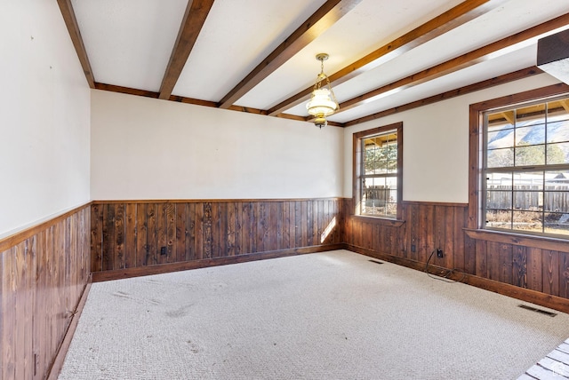 carpeted empty room with beamed ceiling and wood walls