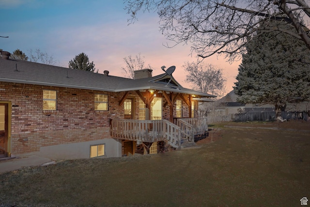 back house at dusk with a deck and a lawn