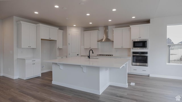 kitchen featuring wall chimney exhaust hood, stainless steel oven, white cabinetry, a sink, and built in microwave