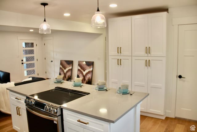 kitchen featuring white cabinetry, decorative light fixtures, a center island with sink, and electric range
