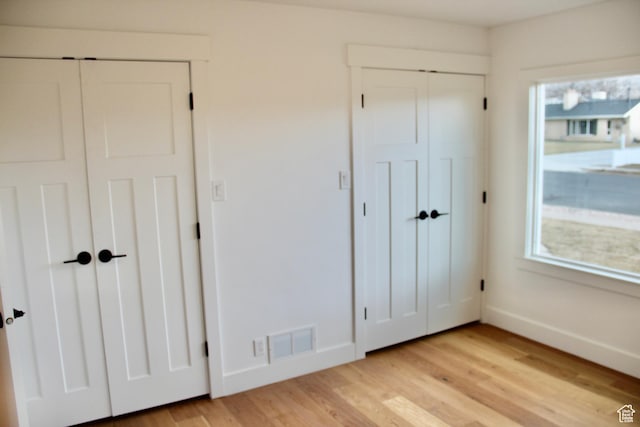 unfurnished bedroom with light wood-type flooring and two closets