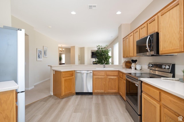 kitchen with appliances with stainless steel finishes, a sink, a peninsula, light wood-style flooring, and light countertops