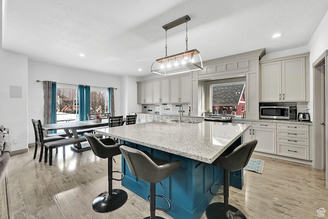 111 S 2300 W, Kaysville, UT 84037 - kitchen featuring decorative backsplash, light wood-style floors, a kitchen breakfast bar, a sink, and appliances with stainless steel finishes