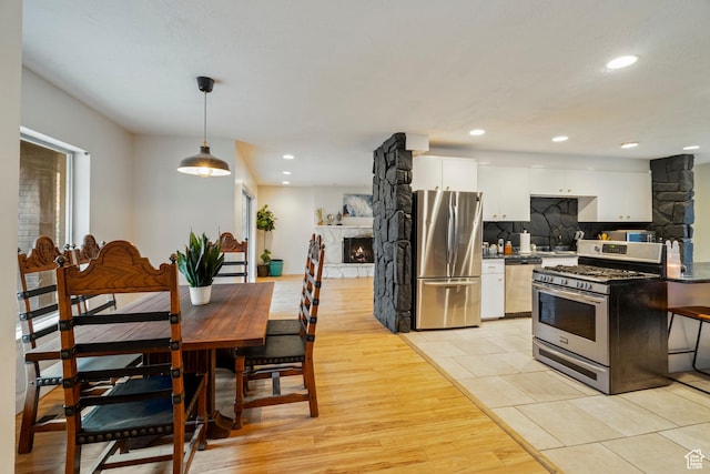 1078 Sumac Dr, Logan, UT 84321 - kitchen featuring white cabinetry, hanging light fixtures, stainless steel appliances, a fireplace, and backsplash
