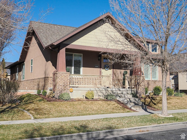 bungalow-style home featuring brick siding, roof with shingles, a front yard, and covered porch