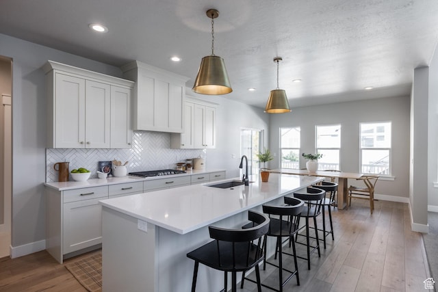 7288 W Hall Crossing Dr S, Herriman, UT 84096 - kitchen with stainless steel gas cooktop, light countertops, decorative backsplash, a kitchen island with sink, and recessed lighting