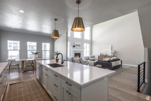 7288 W Hall Crossing Dr S, Herriman, UT 84096 - kitchen featuring a lit fireplace, light countertops, light wood-style flooring, decorative light fixtures, and stainless steel dishwasher