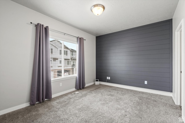 carpeted empty room featuring wood walls, baseboards, a textured ceiling, and visible vents