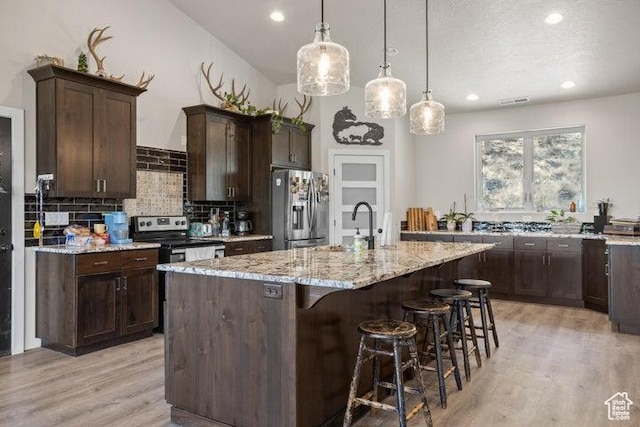 711 W Main St, Enterprise, UT 84725 - kitchen with dark brown cabinetry, hanging light fixtures, appliances with stainless steel finishes, light stone countertops, and a kitchen island with sink