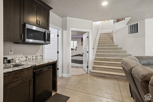 711 W Main St, Enterprise, UT 84725 - kitchen featuring dishwasher, sink, light stone counters, dark brown cabinetry, and a textured ceiling