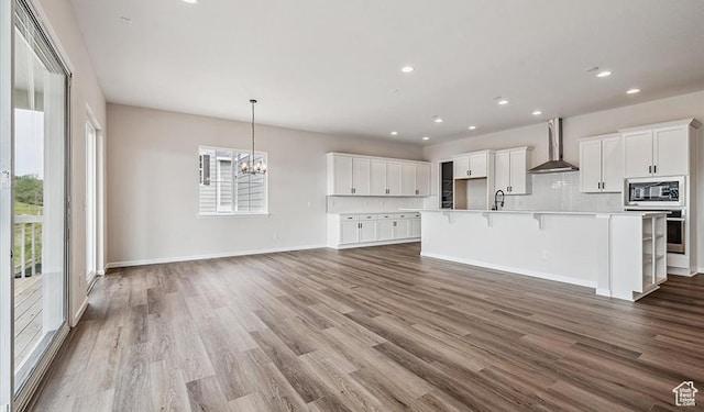 6187 W Wapiti Ridge Ln Unit 334, Herriman, UT 84096 - kitchen with built in microwave, wall chimney exhaust hood, a breakfast bar area, white cabinetry, and a large island with sink