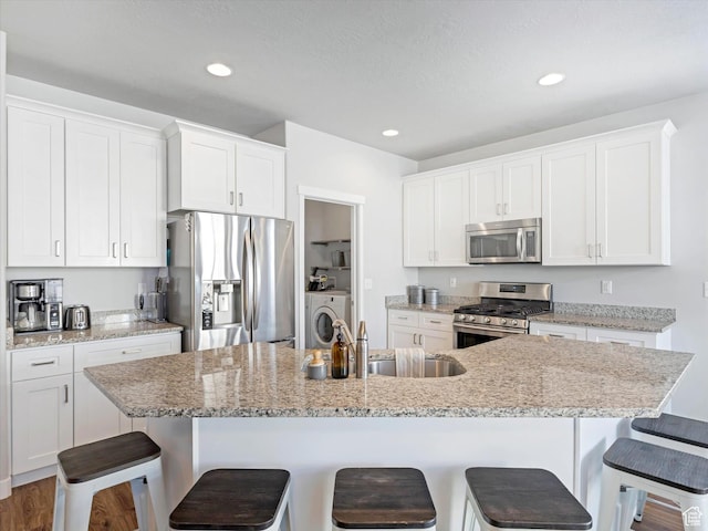 kitchen featuring stainless steel appliances, a breakfast bar, a kitchen island with sink, and white cabinets