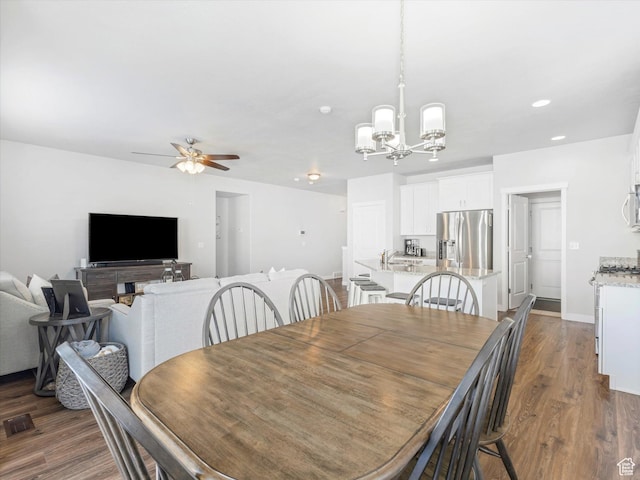 dining space featuring sink, ceiling fan with notable chandelier, and dark wood-type flooring