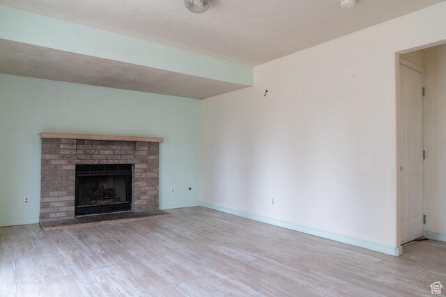 unfurnished living room with a brick fireplace and light hardwood / wood-style flooring