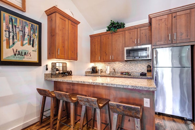 kitchen with lofted ceiling, appliances with stainless steel finishes, dark hardwood / wood-style floors, a kitchen breakfast bar, and decorative backsplash