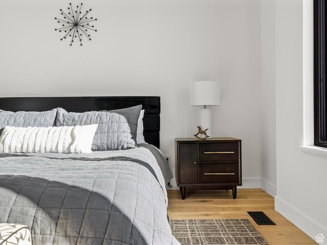 bedroom with baseboards, visible vents, and wood finished floors