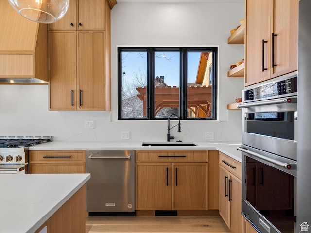 kitchen featuring stainless steel appliances, open shelves, light countertops, a sink, and light wood-type flooring