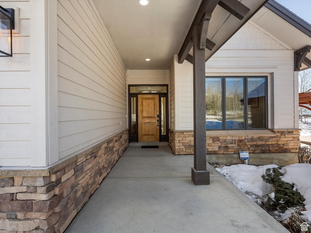 snow covered property entrance with stone siding