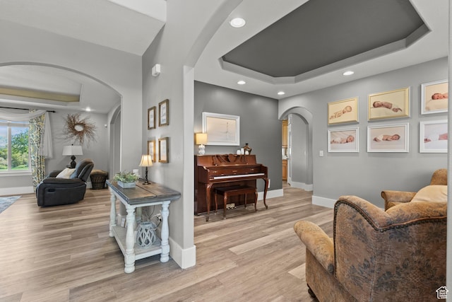 interior space with a tray ceiling, recessed lighting, baseboards, light wood finished floors, and arched walkways