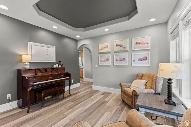 sitting room featuring light wood finished floors, a raised ceiling, arched walkways, and recessed lighting