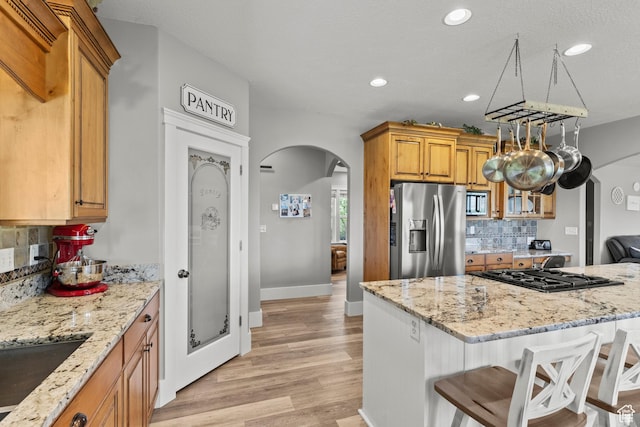 kitchen featuring a kitchen bar, stainless steel appliances, light stone countertops, arched walkways, and backsplash