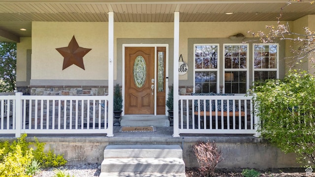 doorway to property featuring covered porch, stucco siding, and stone siding