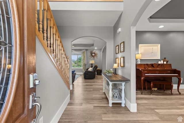 foyer entrance featuring stairs, arched walkways, baseboards, and wood finished floors