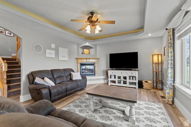 living area with a tray ceiling, a healthy amount of sunlight, wood finished floors, and ceiling fan