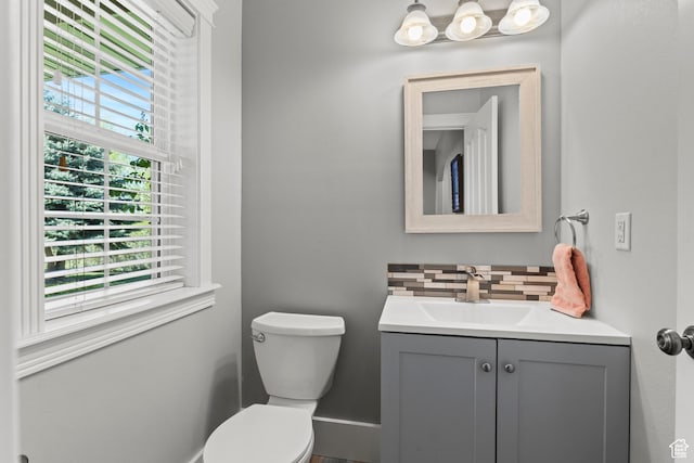half bath with toilet, baseboards, vanity, and decorative backsplash