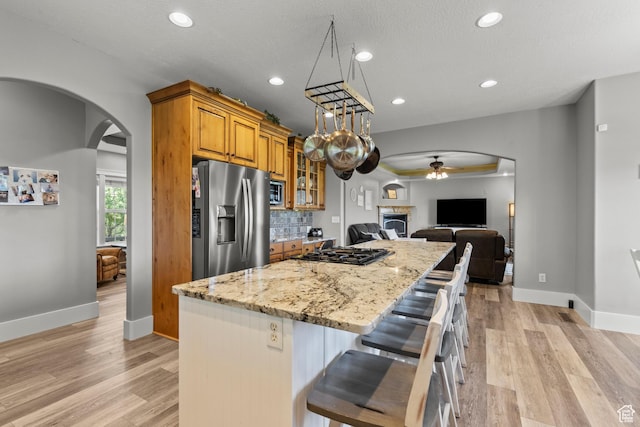 kitchen with stainless steel fridge, a ceiling fan, brown cabinetry, arched walkways, and gas cooktop