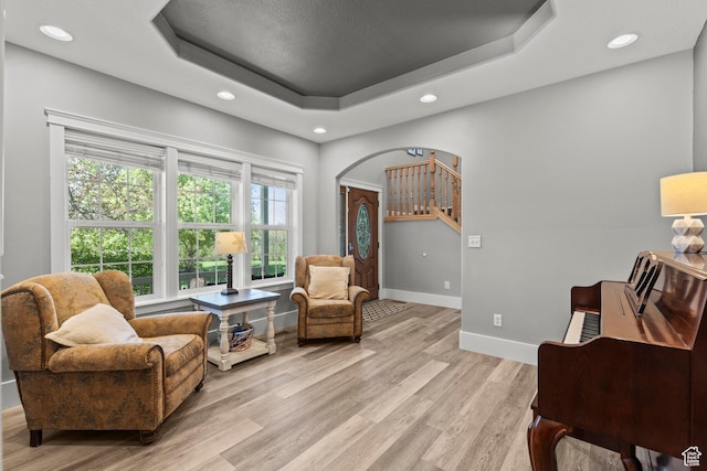 sitting room with light wood-style floors, baseboards, a raised ceiling, and recessed lighting