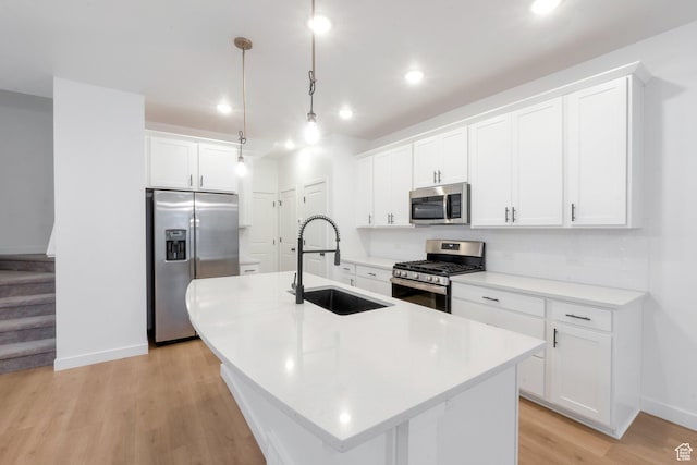 kitchen with light wood-style flooring, a sink, appliances with stainless steel finishes, baseboards, and a center island with sink