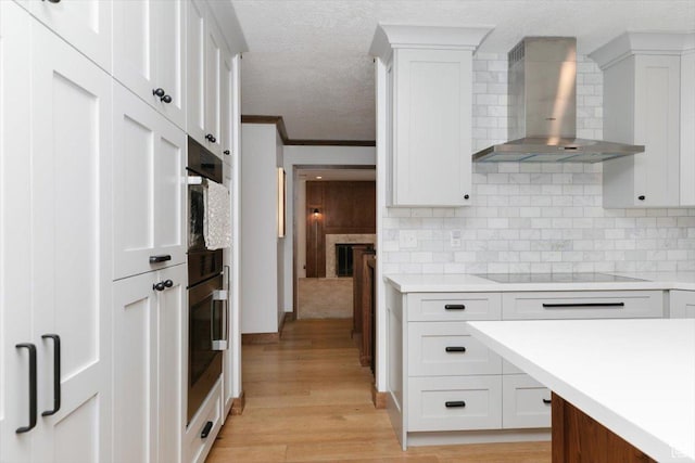 1453 E 1200 N, Logan, UT 84341 - kitchen featuring wall chimney range hood, black electric stovetop, light countertops, light wood finished floors, and a textured ceiling