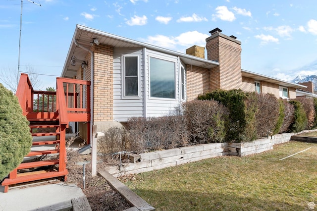 view of side of home with brick siding, a chimney, stairs, and a yard