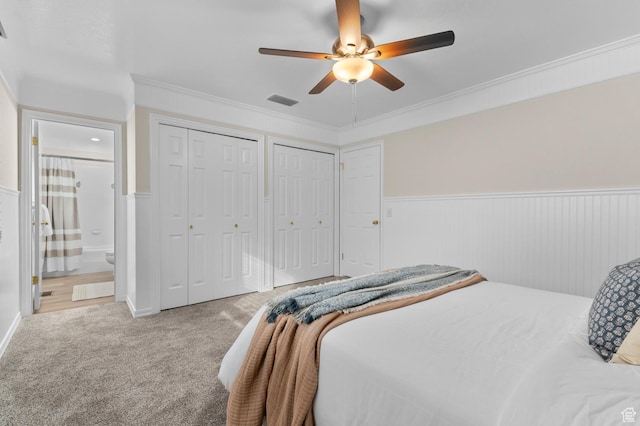 carpeted bedroom featuring a ceiling fan, visible vents, two closets, and wainscoting