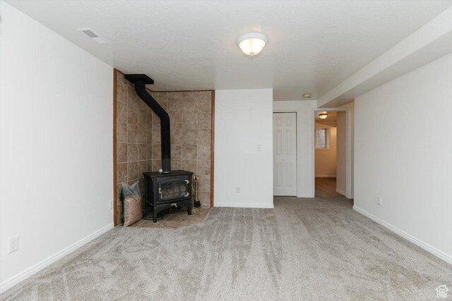 unfurnished living room featuring a textured ceiling, light carpet, and a wood stove